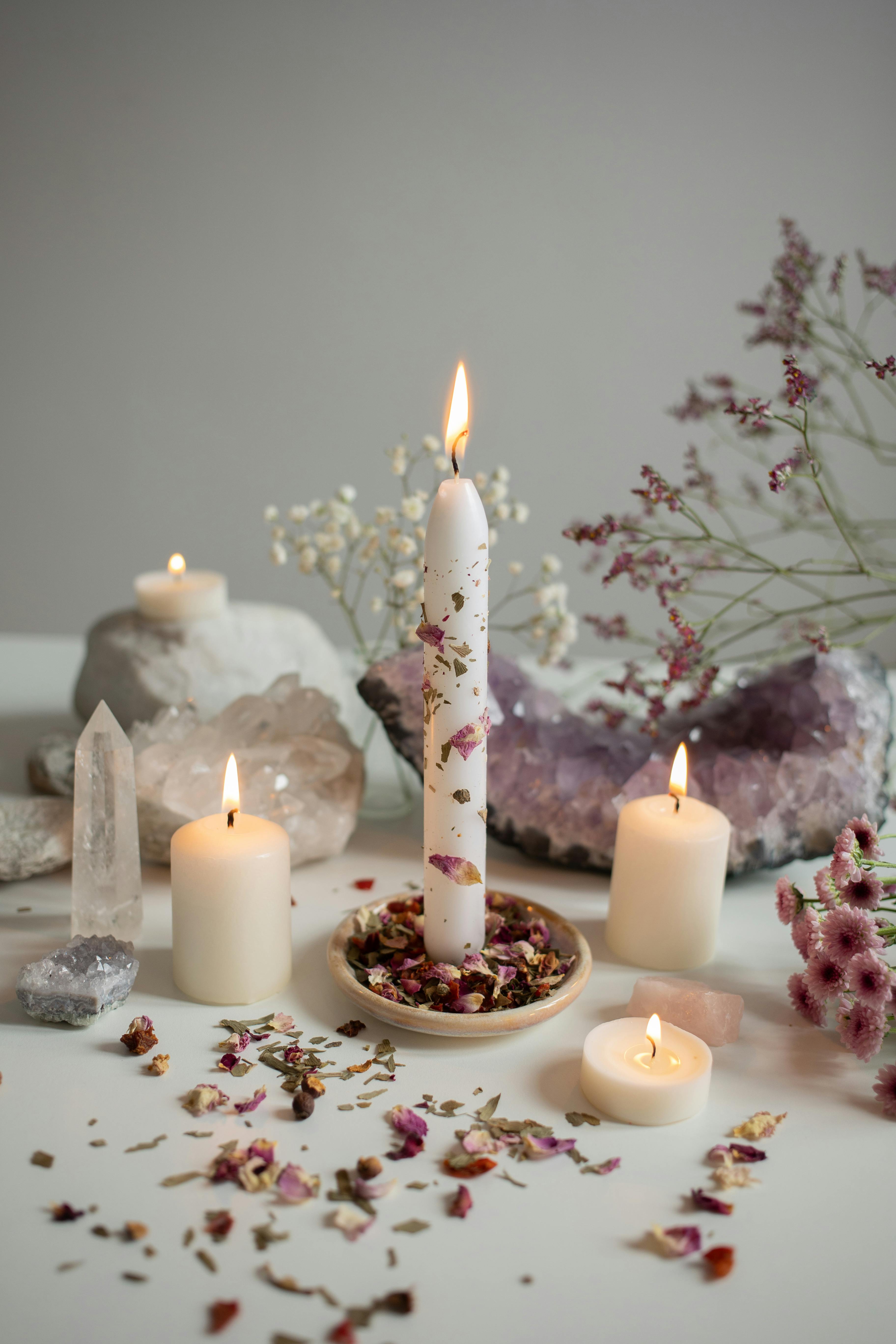 selection of lit candles with aesthetic rose petals and crystals in background