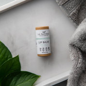 birds eye view shot of lip balm in brown and blue packaging in white backdrop with grey towel and green leaf for aesthetic