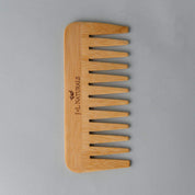 birds eye view shot of Wide Tooth Bamboo Detangling Comb side angle in whitish grey backdrop