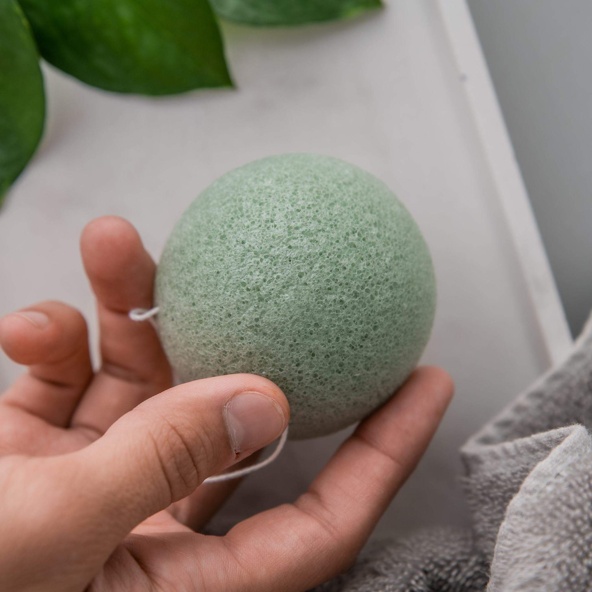 Biodegradable Konjac Sponge teal coloured close up shot held by a male hand in a white backdrop