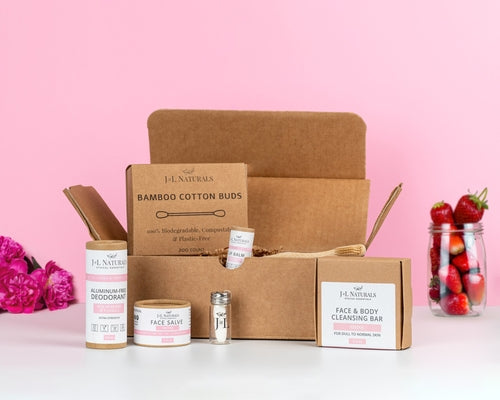 essentials kit with face and skin products in brown and pink packaging with bright pink background and strawberries to add aesthetic