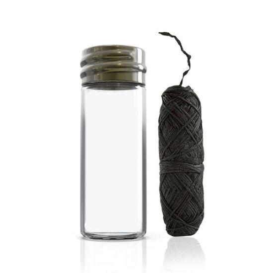 Biodegradable black Charcoal Dental Floss next to empty glass bottle with a white background