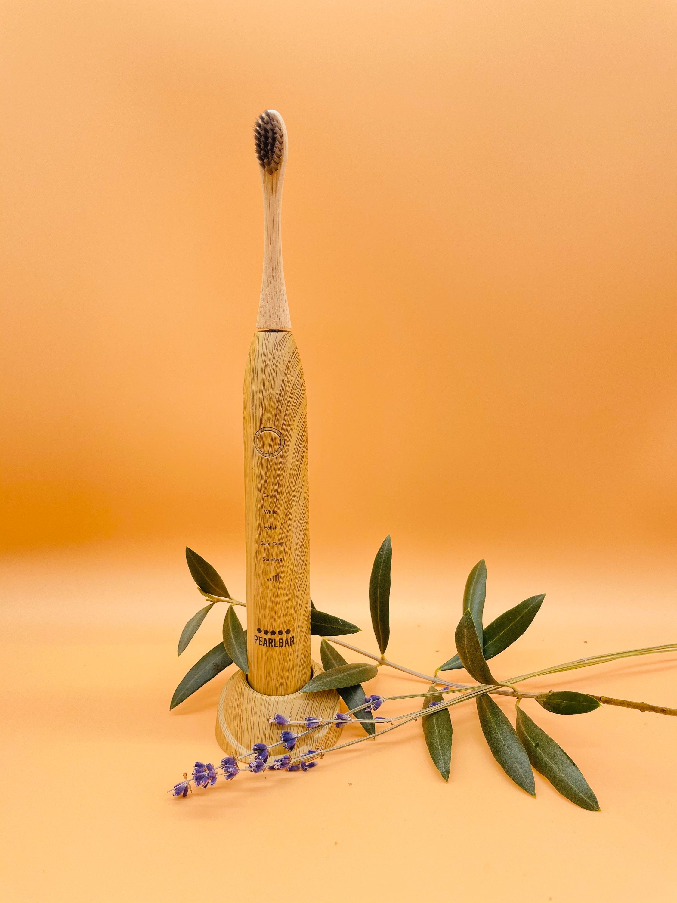 eco friendly bamboo electric toothbrush with a leaf and some lavender in a well lit orange background