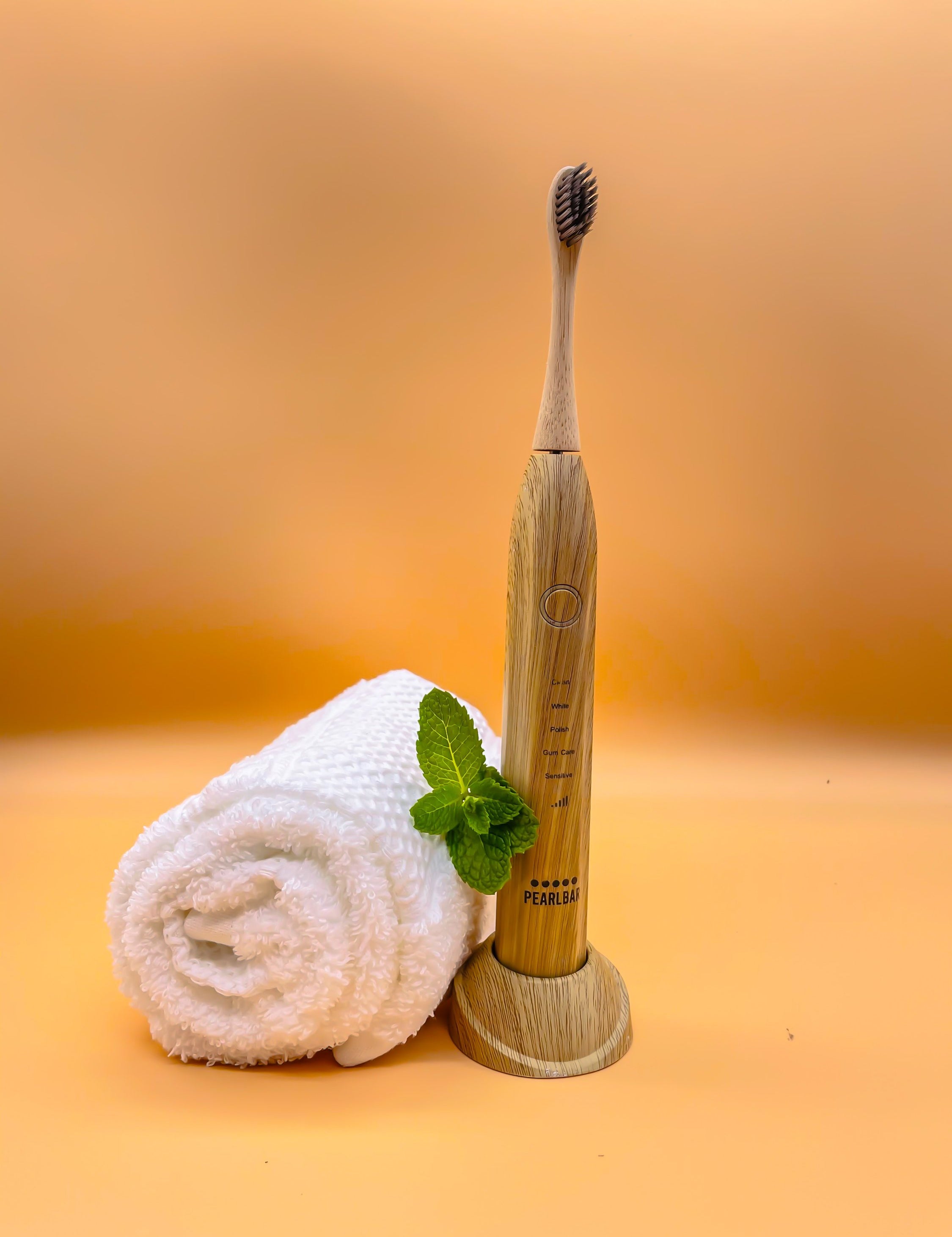 eco friendly bamboo electric toothbrush with a white towel and a leaf in a well lit orange background