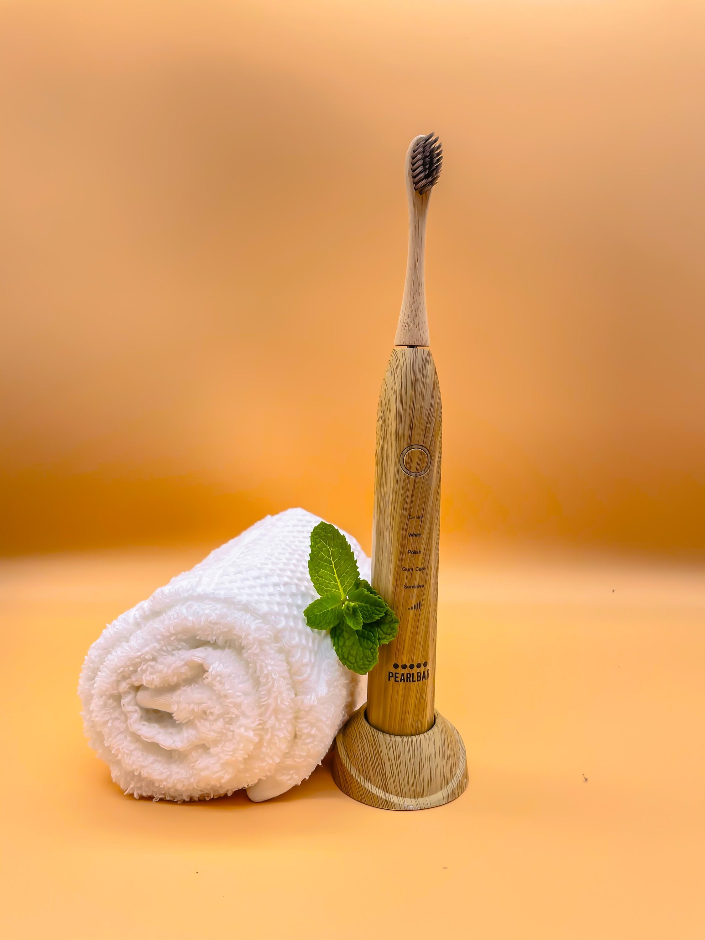 eco friendly bamboo electric toothbrush with a white towel and a leaf in a well lit orange background