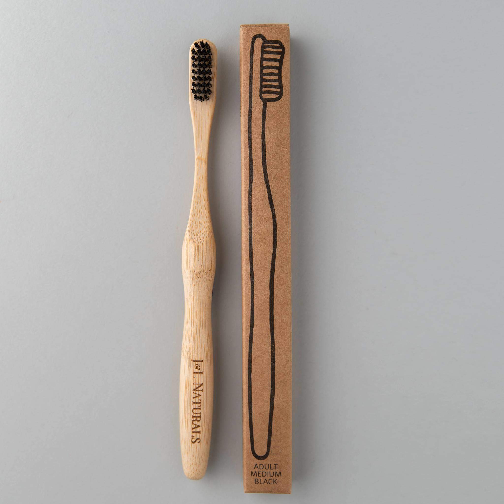 eco friendly bamboo toothbrush with charcoal bristles next to brown packaging in white background