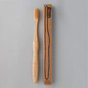 eco friendly bamboo toothbrush with skin coloured charcoal bristles next to brown packaging in white background