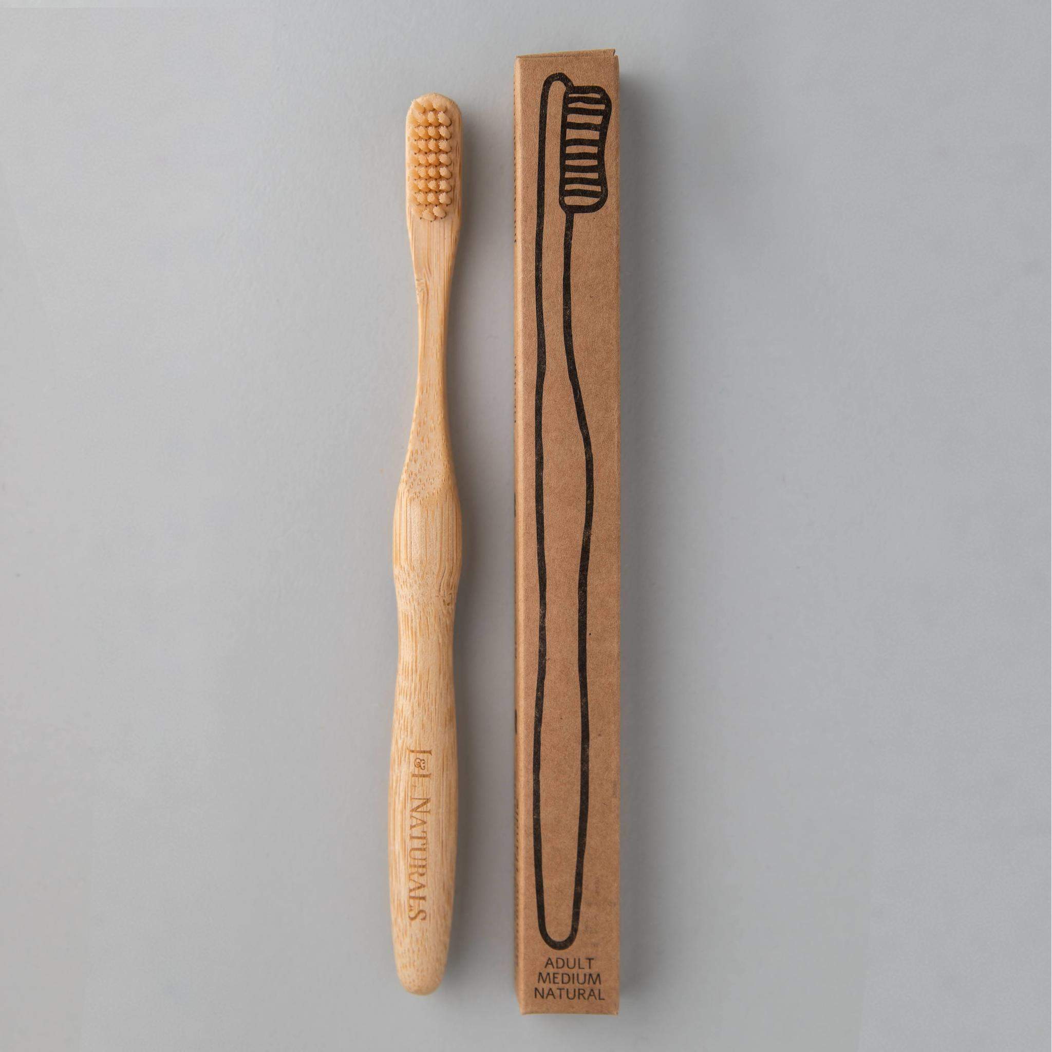 eco friendly bamboo toothbrush with skin coloured charcoal bristles next to brown packaging in white background