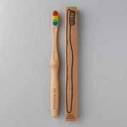 eco friendly bamboo toothbrush with rainbow coloured charcoal bristles next to brown packaging in white background