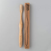 eco friendly bamboo toothbrush with white charcoal bristles next to brown packaging in white background