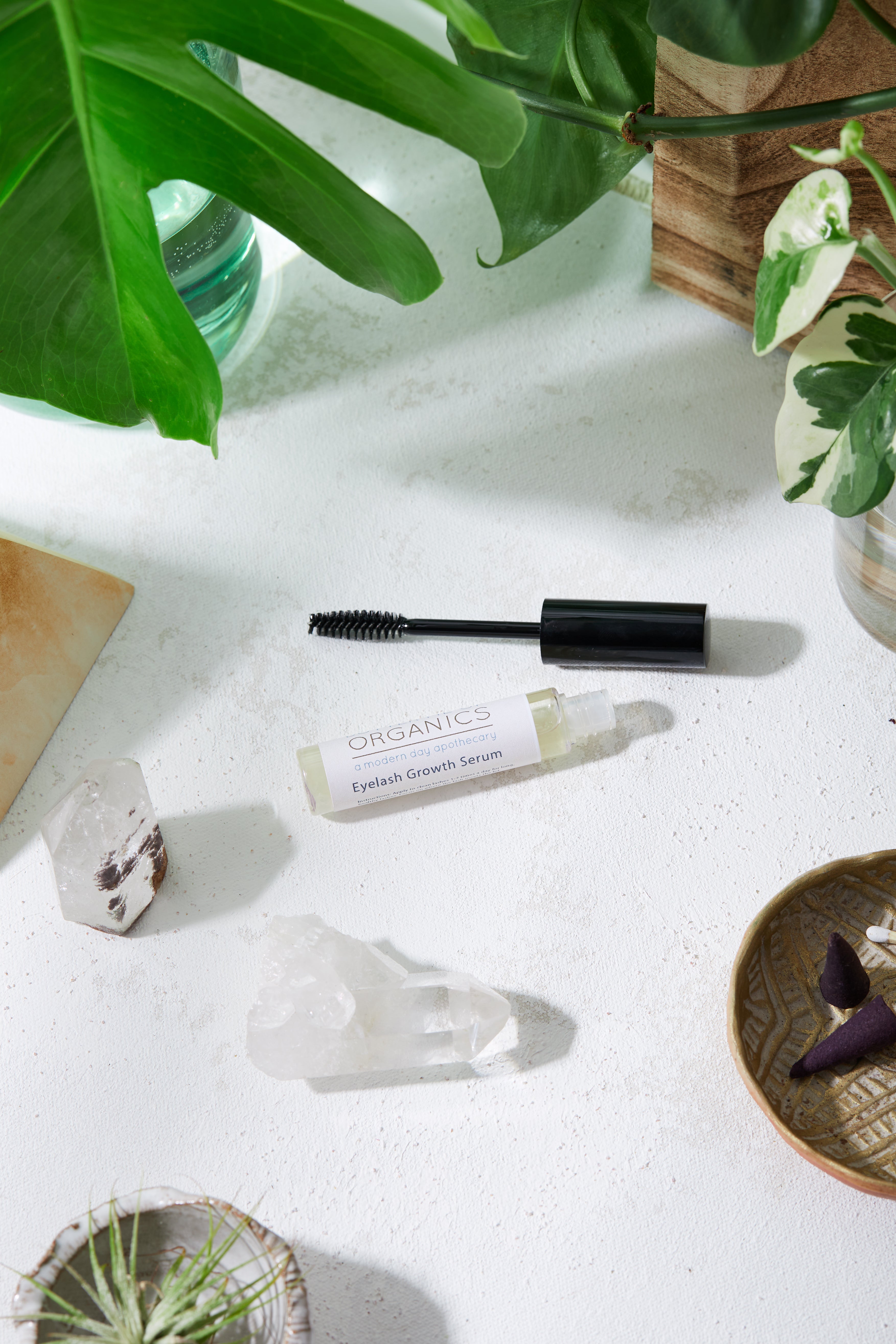 Natural Organic Eyelash Growth Serum in aesthetic white background with one crystal and green leaf for aesthetics slightly zoomed out shot