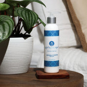 naturally scented body lotion in plastic neutral certified white blue bottle on wood table with a leaf and white bed in backdrop