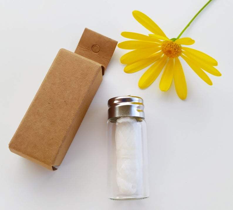 Biodegradable White Charcoal Dental Floss in glass bottle with a white background brown box and a yellow flower