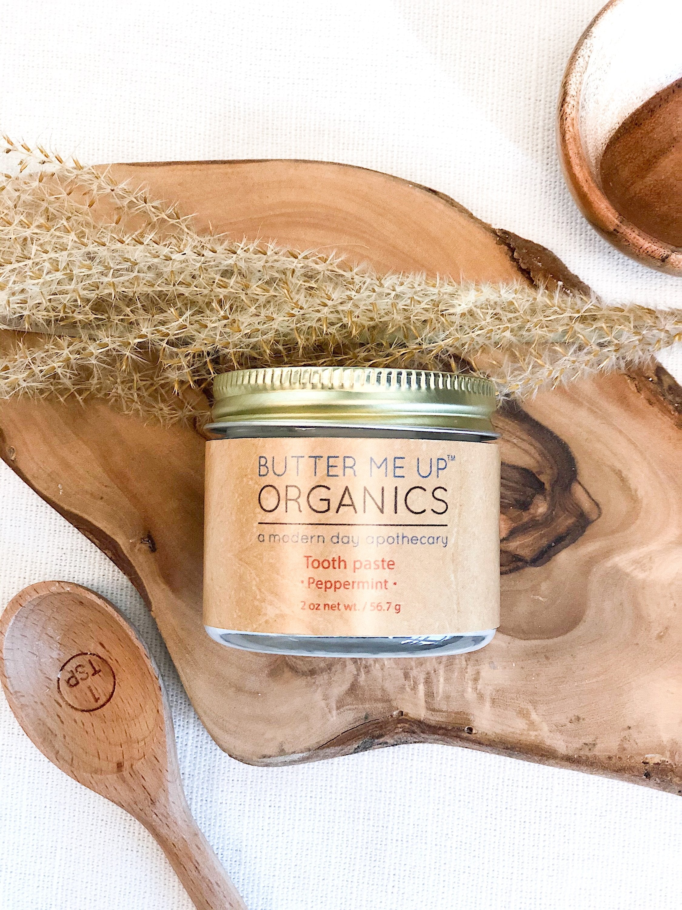 birds eye view shot of closed toothpaste powder in glass jar tin accompanied with wooden spoon and leaves for aesthetic in white backdrop